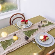 the table is set for christmas dinner with pine cones and candles on it, along with two wine glasses