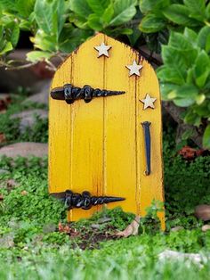 a small yellow door with stars on it in the middle of some grass and bushes