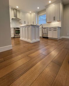 an empty kitchen with white cabinets and wood floors