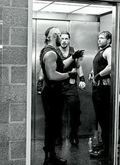 two men standing in front of an elevator talking to each other while one man is holding his hand out