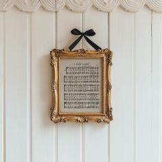 a framed musical score with a black bow hanging on the wall next to white wood paneling