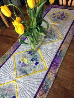 a vase filled with yellow flowers sitting on top of a table covered in quilts