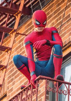 a spider man statue sitting on top of a metal railing next to a brick building