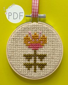 a cross stitch pattern with a flower in the center on a yellow background that is framed by a pink and white checkered ribbon