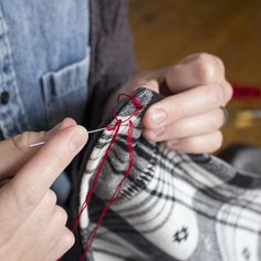 a woman is knitting something with red yarn on her hand and the thread has been pulled through