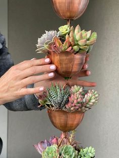 a woman's hand is reaching up into a stack of succulents