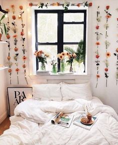 a bed with white comforter and flowers on the wall next to a large window