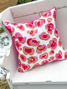 a pink and gold pillow sitting on top of a white chair