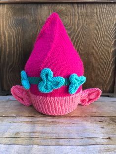 a pink knitted hat with blue bows on it's brim sits against a wooden background