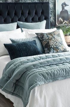 a bed with blue and white comforters in a bedroom next to a painting on the wall