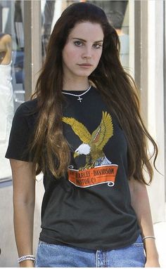 a woman with long hair and an eagle t - shirt is walking down the street