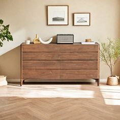 a wooden dresser sitting in the corner of a living room next to a plant and pictures on the wall