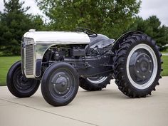 an old - fashioned tractor is parked on the sidewalk in front of some trees and grass