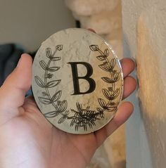 a person holding up a round badge with the letter b on it's side