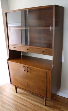 a wooden cabinet sitting on top of a hard wood floor next to a white wall