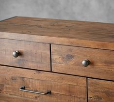 a wooden dresser with three drawers and two knobs on each drawer, against a gray background