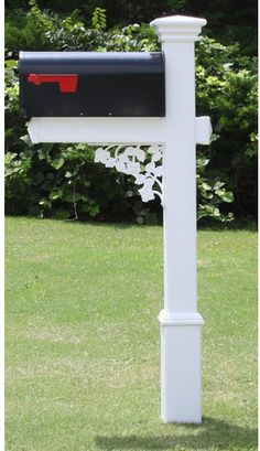 a white mailbox in the middle of a grassy area with trees and bushes behind it