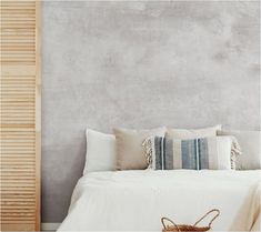 a bed with white linens and pillows in front of a gray wall, next to a wooden slatted door