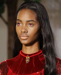 a model with long hair and red eyes wearing a red velvet dress on the runway