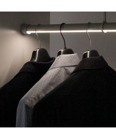 two shirts are hanging on a rail in front of a wall with a light behind them