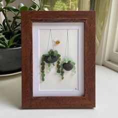 a wooden frame with some plants and rocks hanging from it's sides in front of a potted plant