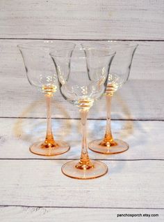 three wine glasses sitting next to each other on a white tablecloth covered floor with wood planks