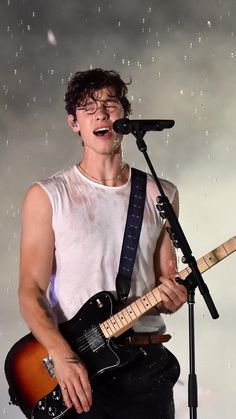 a young man singing into a microphone while holding an electric guitar in front of him