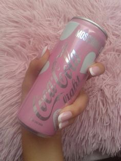 a woman's hand holding a pink can of coca - cola on top of a fluffy pink carpet