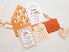 the wedding stationery is laid out on top of each other, including an orange and white envelope