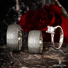 two gold rings sitting on top of a rock next to a red rose