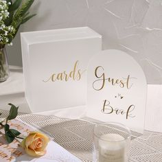 two cards and a candle on a table with flowers in vases next to it