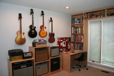 guitars and amps are lined up on the wall in this music room with bookshelves