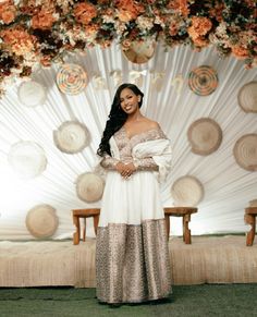 a woman standing in front of a backdrop with flowers on it and wearing an off the shoulder dress