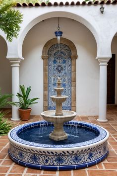 a blue and white fountain in the middle of a courtyard with potted plants next to it