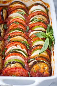 a casserole dish filled with sliced vegetables and garnished with basil leaves