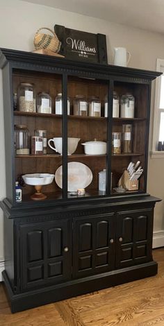 an old black china cabinet with glass doors and plates on it's top shelf