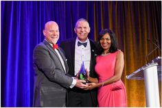 two men and a woman standing next to each other in front of a podium holding an award