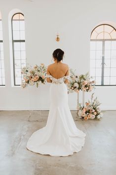 the back of a bride's wedding dress in front of floral arrangements and windows