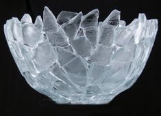 a clear glass bowl with small pieces of ice in it's center, on a black background