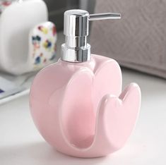 a pink soap dispenser sitting on top of a white counter next to a laptop