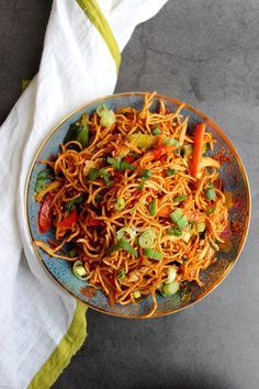 a blue plate topped with noodles and veggies on top of a white towel