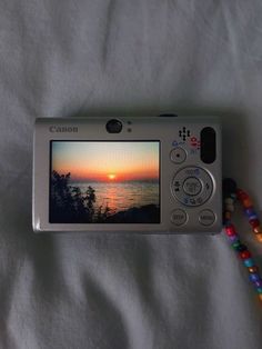 a digital camera sitting on top of a bed next to beaded bracelets and beads