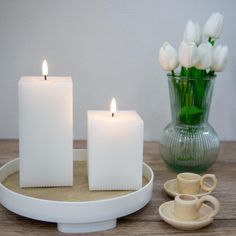 two white candles sitting on top of a table next to a cup and saucer