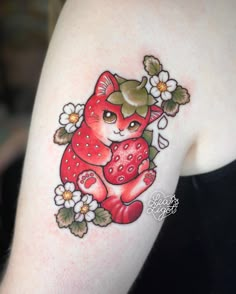 a woman's arm with a red cat and flowers on it, holding a strawberry