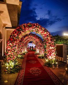 an archway decorated with red flowers and greenery at night, lit up by candles