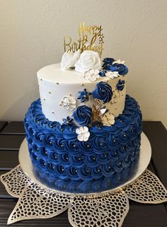 a blue and white birthday cake with flowers on the top is sitting on a doily