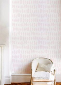 a white chair sitting in front of a wall with a pink pattern on the wall