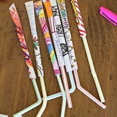 several colorful paper straws are lined up on a wooden table with markers and pens