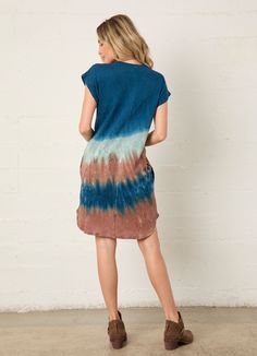 a woman standing in front of a white wall wearing a blue and brown tie dye dress