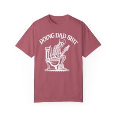 ✨💀 Introducing our "Doing Dad Shit" Skeleton T-Shirt! 💀✨ 🎉 Celebrate Father's Day with a humorous twist by gifting this custom tee featuring a skeleton on a toilet and the phrase, "Doing Dad Shit"! 🎉 💖 Crafted from 100% ring-spun cotton, this garment-dyed t-shirt offers unbeatable softness and comfort, perfect for everyday wear. 💖 😌 The soft-washed fabric adds an extra layer of coziness, making this tee an ideal choice for dads who appreciate both comfort and humor. 😌 💪 With double-needle stitching throughout, this tee is built to last, ensuring durability for all of dad's adventures. 💪 🔄 Say goodbye to bothersome side-seams – our shirt maintains its tubular shape for a sleek and flattering fit. 🔄 🎨 Show your appreciation with this fully customizable design featuring a playful Novelty Cotton T-shirt With Screen Print, Father's Day T-shirt With Funny Print, Novelty Screen Print T-shirt For Streetwear, Novelty Screen Print Streetwear T-shirt, Novelty Streetwear T-shirt With Screen Print, Funny Screen Print T-shirt For Father's Day, Father's Day T-shirt With Funny Print In Relaxed Fit, Funny Relaxed Fit Pre-shrunk T-shirt, Funny Father's Day T-shirt With Screen Print